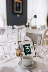 Wedding. Banquet. On festive tables with white tablecloths there are compositions of flowers, candles, cutlery, glasses, plates, menu cards and name plates