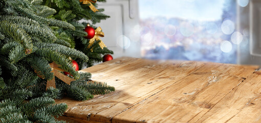 A wooden table with a green Christmas tree and an open door against the background of a blurred landscape, free space