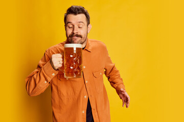 Portrait of emotive handsome man in orange shirt posing with lager foamy beer glass isolated over...