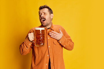 Portrait of emotive handsome man in orange shirt posing with lager foamy beer glass isolated over...
