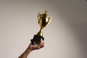Raised hands of old man holding trophy. Isolated, close up.