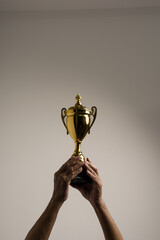 Raised hands of old man holding trophy. Isolated, close up.