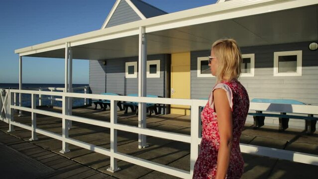 Blonde caucasian woman walking at famous Busselton wooden jetty in Busselton, Western Australia with sunset light. Female tourist in iconic place. Summer and holidays season.
