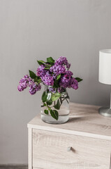 A bouquet of lilacs in a glass vase and a lamp.