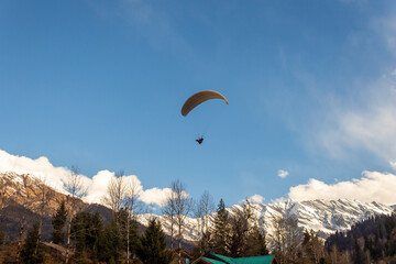 Manali Paragliding in the blue sky with snow mountains of Manali in Himachal Pradesh. Panoramic views of Himalayas. Natural beauty of Solang Valley. Manali Himachal Pradesh. Rohtang Pass Snow winters.