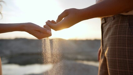 The hands of a young girl and a guy pour sand from the beach at sunset. Sea sand in a man's hand. man's hand holds sand. Sand falls out of your hands. Male and female hands pour sand.