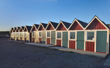 Fototapeta na wymiar swedish traditional beach cabins aligned at the sea side under blue sky and sunset light