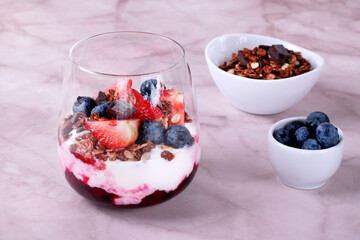 Yogurt with chocolate granola and cherry sauce topped with strawberry and blueberry served in a glass. Healthy breakfast