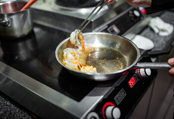 man chef cooking tasty shrimp in frying pan on kitchen