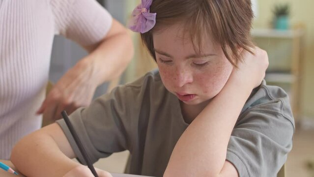 14 year old girl with down syndrome drawing on sheet of paper together with mother spending leisure time at home