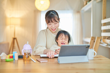 自宅でタブレットPCを操作する女性と泣く幼児