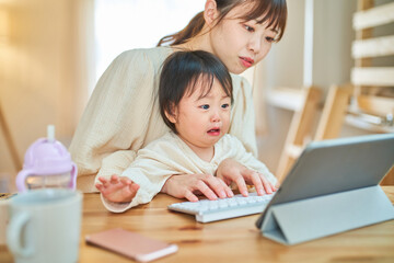 自宅でタブレットPCを操作する女性と泣く幼児