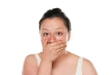 Young shocked chubby woman covering her mouth with her hand on white background.