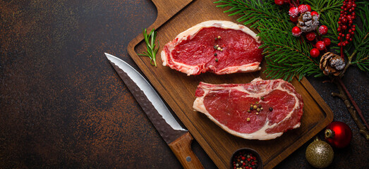 Two raw uncooked meat beef steaks on wooden cutting board with knife and seasonings on dark rustic...