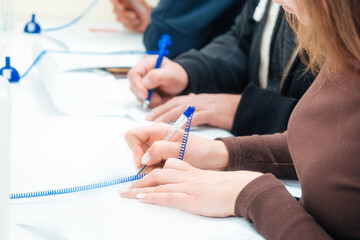 Woman fills out blank application form at table or signs contract. Hands of people with close-up fountain pen. Perspective view Several people simultaneously fill in data with pen on paper..