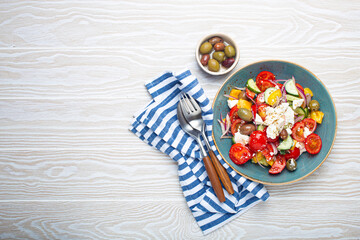 Obraz na płótnie Canvas Greek fresh healthy colorful salad with feta cheese, vegetables, olives in blue bowl on rustic white wooden background top view, Mediterranean diet, traditional cuisine of Greece. Space for text
