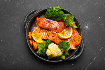 Healthy baked fish salmon steaks, broccoli, cauliflower, carrot in cast iron casserole bowl black...