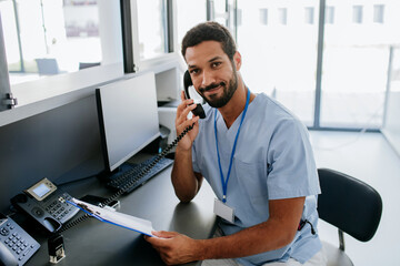 Portrait of young multiracial doctor sitting at reception and calling.