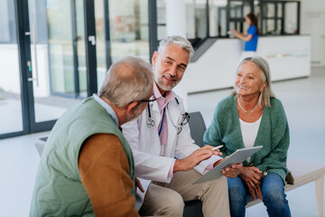 Obraz premium Mature doctor talking with his senior patients at hospital corridor.