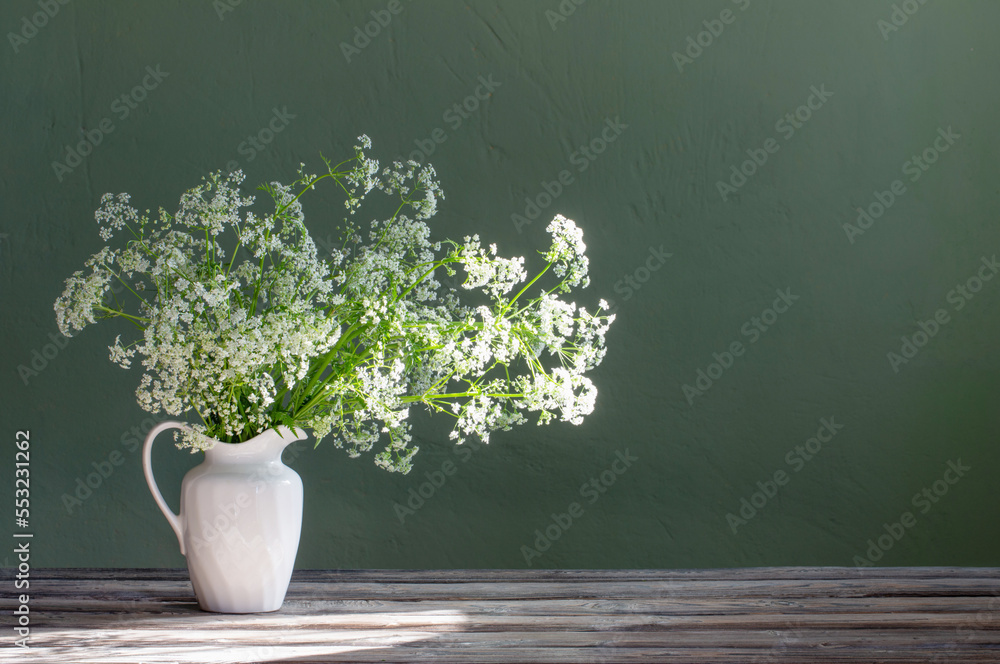 Wall mural white wild flowers in jug on background green wall