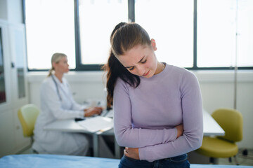 Teenage girl with stomach ache sitting in doctor's office.