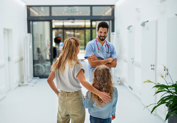 Young multiracial doctor talking with mother of little girl at hospital corridor.