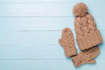 Brown winter hat and mittens on wooden background. Top view