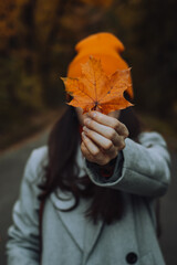 Young woman is holding a maple leaf in front of her face by covering it