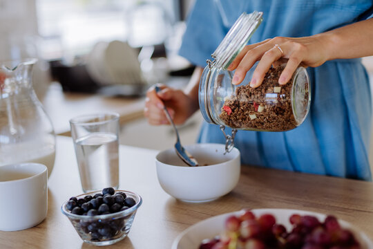 Close-up of young woman preparing muesli for breakfast in her kitchen, morning routine and healthy lifestyle concept.