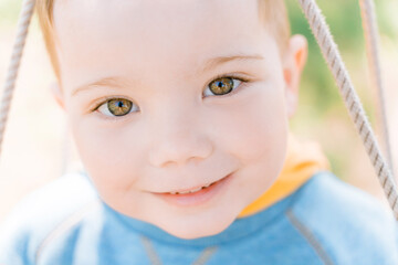 Сlose-up portrait of a cute green-eyed boy of three years looking with interest and smiling - obrazy, fototapety, plakaty
