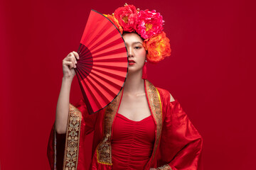Young asian woman wearing qipao cheongsam dress with Chinese folding fan on red background for...