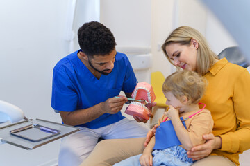 Young multiracial dentist showing little girl how to clean teeth.