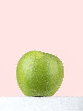 Bottom view of a green apple against a pink background.