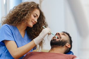 Young woman dentist doing doing preventive examination to multiracial man. © Halfpoint