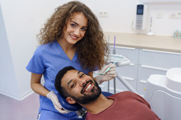 Young woman dentist doing doing preventive examination to multiracial man.