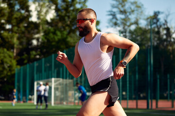 Side view of a male athlete sprinting on a running track in a track and field stadium holding a...