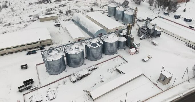 flight over agro silos granary elevator in winter day in snowy field. Silos on agro-processing manufacturing plant for processing drying cleaning and storage of agricultural products