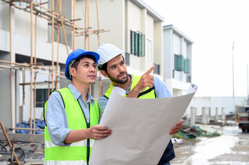 Construction engineer and architect check plan working with the blueprint on construction site. They are in safety vests with helmets for safety. Construction project concept.