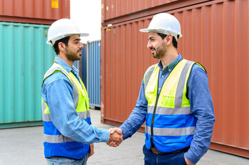 Two engineer container cargo wearing white hardhat and safety vests in successful handshake together at container yard. success in logistics business import export industry