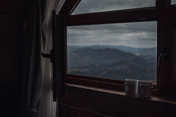 Fototapeta premium Two cups of tea on windowsill with opened window in front of mountains view