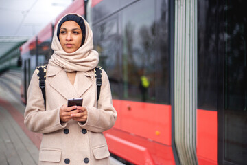 Young muslim woman with smartphone getting off the tram.