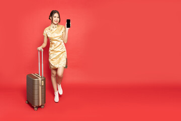Asian woman traveler wearing red traditional cheongsam qipao dress drag luggage and showing mobile phone isolated on red background, Tourist girl having cheerful holiday trip concept