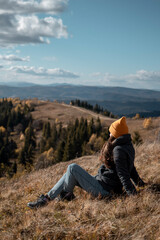 Naklejka na ściany i meble Young tourist woman is sitting on ground and enjoying mountains landscape