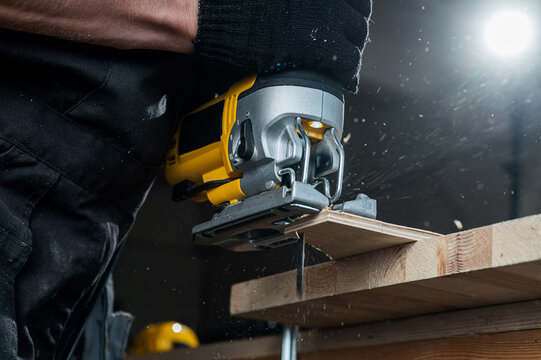 Close-up of a man cutting a wooden plank with an electric jigsaw in a workshop.