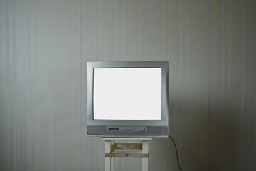 Empty white monitor of vintage tv standing on wooden stool inside of house room with old wallpaper
