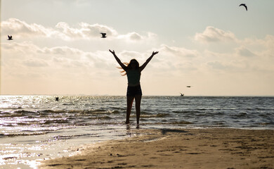 girl playing on the beach with her arms in the air reaching for the sky