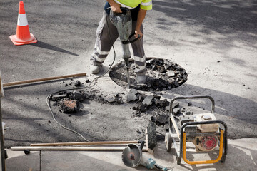 jackhammer in the hands of asphalt worker preparing logs underground