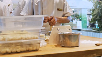 The chef in the kitchen prepares the dough for a delicious dish from Italian cuisine. The cook tears off pieces of dough for making dumplings. Baker working with dough in the kitchen