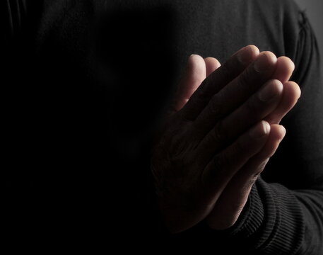 man praying to god with hands together Caribbean man praying with black background stock photo