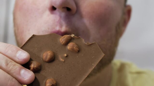 A man eats appetizingly natural chocolate with a nut, a portrait of a man eating milk chocolate close-up. Man biting a bar of chocolate with his teeth